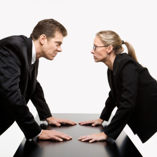 Caucasian mid-adult businessman and woman staring at each other with hostile expressions.